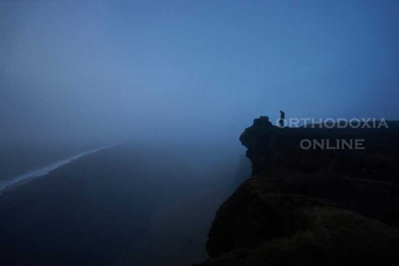 person standing rock cliff covered with fog