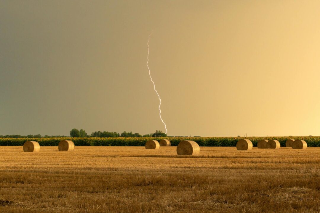 a lightning above a field with hay bales